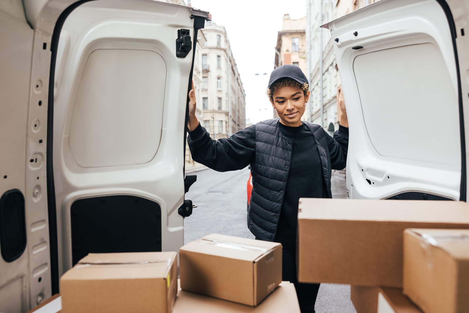 Female courier opening a car trunk doors and looking on cardboard boxes