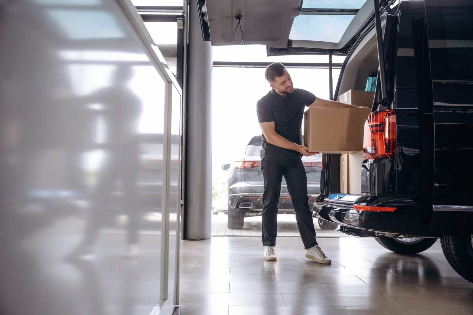 Holding the packed product in hands. Delivery man or loader is near the car with a box.