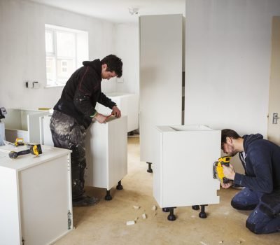 Two builders, building white kitchen units.